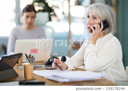 Adult woman judging female colleague talking on mobile phone Adult woman judging female colleague talking on mobile phone 139176244