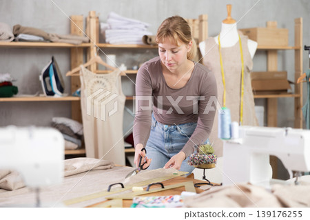 Young female dressmaker cutting textile in sewing workshop Young female dressmaker cutting textile in sewing workshop 139176255