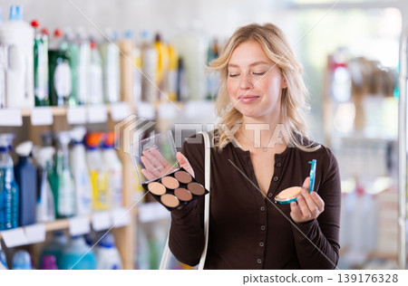 Beautiful young girl pondering and choosing face powder in cosmetics department in supermarket Beautiful young girl pondering and choosing face powder in cosmetics department in supermarket 139176328