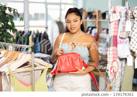 Undetermined young girl choosing handbag in clothing store Undetermined young girl choosing handbag in clothing store 139176361