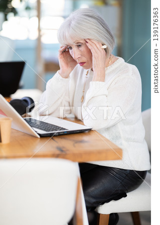 Elderly businesswoman suffers from headaches while working in office Elderly businesswoman suffers from headaches while working in office 139176363