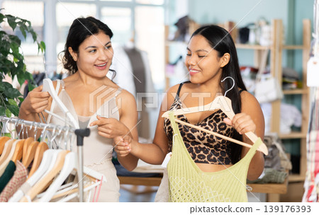 Two young women choosing summer dresses or tops in clothing store Two young women choosing summer dresses or tops in clothing store 139176393