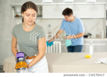 Girl collects dust with vacuum cleaner during group cleaning in kitchen Girl collects dust with vacuum cleaner during group cleaning in kitchen 139176417