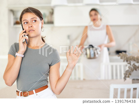 Upset daughter is sitting at table. Mom yells at her daughter in background 139176438