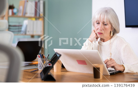 Senior woman working in office, using laptopat workplace. Senior woman working in office, using laptopat workplace. 139176439