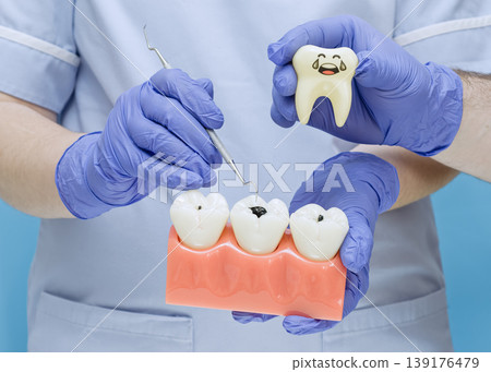 Dentist holding a sad crying tooth toy and a dental model with visible cavities. Educational concept for toothache, decay, caries, root canal, and pediatric dentistry. Dentist holding a sad crying tooth toy and a dental model with visible cavities. Educational concept for toothache, decay, caries, root canal, and pediatric dentistry. 139176479