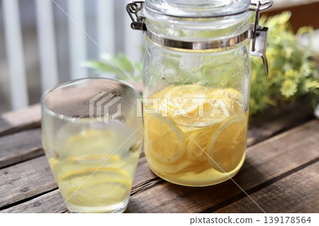 A bottle of homemade lemon syrup and hot lemonade placed on the windowsill. A bottle of homemade lemon syrup and hot lemonade placed on the windowsill. 139178564