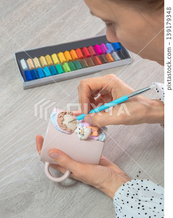 Woman paints delicate design on pink ceramic mug Woman paints delicate design on pink ceramic mug 139179348