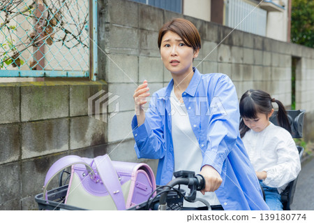 A woman riding a bicycle with an elementary school child on the back. 139180774