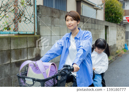 一名女子騎著腳踏車,後座載著一名小學生。 一名女子騎著腳踏車,後座載著一名小學生。 139180777