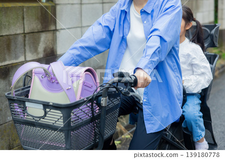 A woman riding a bicycle with an elementary school child on the back. A woman riding a bicycle with an elementary school child on the back. 139180778