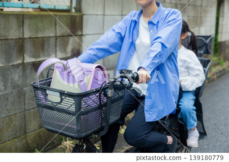 一名女子騎著腳踏車,後座載著一名小學生。 一名女子騎著腳踏車,後座載著一名小學生。 139180779