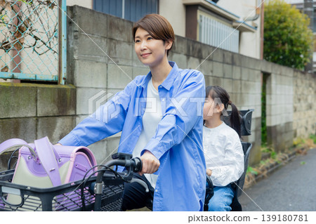 A woman riding a bicycle with an elementary school child on the back. A woman riding a bicycle with an elementary school child on the back. 139180781