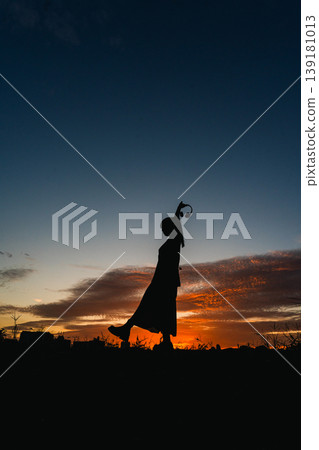 Against the backdrop of a sunset sky, the silhouette of a woman, empowered by music, has resolved to take a step forward. 139181013