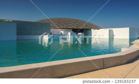 Abu Dhabi, United Arab Emirates - Jan 10 2024, Panoramic view of the snow-white facade of the Louvre Abu Dhabi with a metal dome surrounded by water, at daytime, Abu Dhabi, United Arab Emirates Abu Dhabi, United Arab Emirates - Jan 10 2024, Panoramic view of the snow-white facade of the Louvre Abu Dhabi with a metal dome surrounded by water, at daytime, Abu Dhabi, United Arab Emirates 139183237