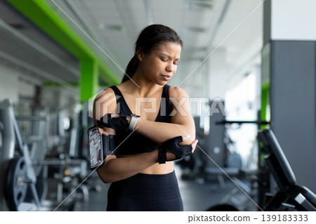 Young Black woman in gym holding her elbow with a pained expression 139183333