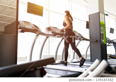 Young Black woman running on treadmill in gym, wearing white headphone Young Black woman running on treadmill in gym, wearing white headphone 139183382