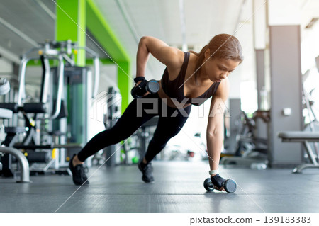 Black woman doing dumbbell renegade row exercise at gym in plank position Black woman doing dumbbell renegade row exercise at gym in plank position 139183383