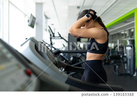 Young Black woman standing on treadmill with hands behind head looking exhausted Young Black woman standing on treadmill with hands behind head looking exhausted 139183388
