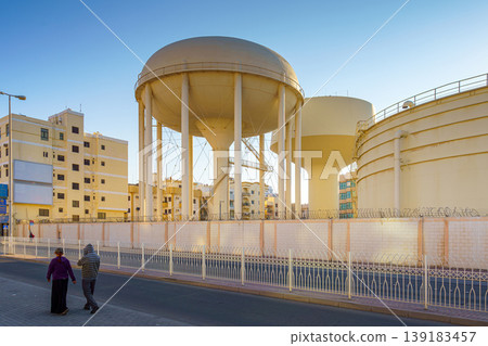 Manama, Bahrain - Jan 08 2024, a Panoramic view of two large beige water towers, a couple of people are walking in the foreground, in the daytime, Manama, Bahrain Manama, Bahrain - Jan 08 2024, a Panoramic view of two large beige water towers, a couple of people are walking in the foreground, in the daytime, Manama, Bahrain 139183457