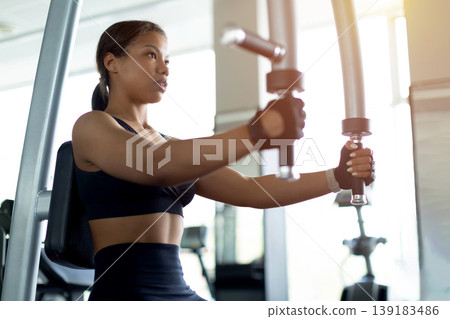 Focused young Black woman using cable machine in gym for chest exercise Focused young Black woman using cable machine in gym for chest exercise 139183486