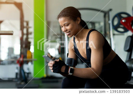 Young Black woman smiling while using smartphone during gym break Young Black woman smiling while using smartphone during gym break 139183503