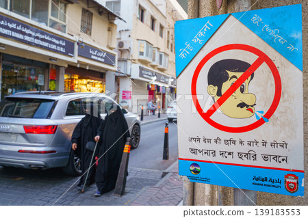 Manama, Bahrain - Jan 08 2024, A view of the street with pedestrians, half of the frame is occupied by a warning sign prohibiting spitting, Manama, Bahrain Manama, Bahrain - Jan 08 2024, A view of the street with pedestrians, half of the frame is occupied by a warning sign prohibiting spitting, Manama, Bahrain 139183553