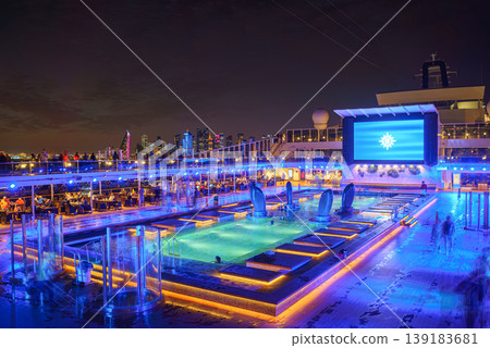 Doha, Qatar - Jan 07 2024, Panoramic view of the deck of the MSC Virtuosa cruise ship with a swimming pool, skyscrapers of Doha are visible in the background, at nighttime, Doha, Qatar Doha, Qatar - Jan 07 2024, Panoramic view of the deck of the MSC Virtuosa cruise ship with a swimming pool, skyscrapers of Doha are visible in the background, at nighttime, Doha, Qatar 139183681