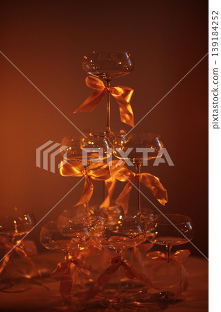 Champagne tower made of glass flutes tied with orange ribbons, illuminated by warm light, creating an elegant display for celebrations or special events Champagne tower made of glass flutes tied with orange ribbons, illuminated by warm light, creating an elegant display for celebrations or special events 139184252
