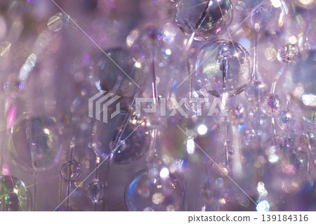 Close-up of translucent glass beads in various sizes reflecting light, creating a shimmering effect against a soft purple background Close-up of translucent glass beads in various sizes reflecting light, creating a shimmering effect against a soft purple background 139184316