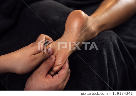 Close-up of a skilled therapist performing a foot massage on a relaxed client, showcasing the soothing technique and the serene atmosphere of a wellness environment 139184341