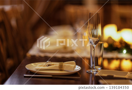 Elegant dining table set with white plates, sparkling glassware, and decorative napkins, creating a warm and inviting atmosphere for a special occasion or celebration Elegant dining table set with white plates, sparkling glassware, and decorative napkins, creating a warm and inviting atmosphere for a special occasion or celebration 139184350