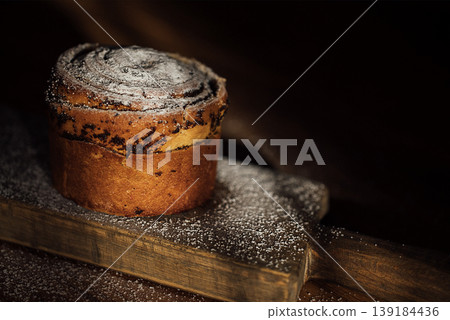 Chocolate swirl pastry dusted with powdered sugar on a wooden board, showcasing rich textures and warm tones in a dimly lit setting 139184436