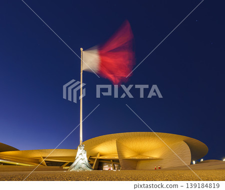 Doha, Qatar - Jan 06 2024, a panoramic view of fluttering Qatar flag in Nation Museum of Qatar, in shape of desert rose, at nighttime with illumination, Doha, Qatar Doha, Qatar - Jan 06 2024, a panoramic view of fluttering Qatar flag in Nation Museum of Qatar, in shape of desert rose, at nighttime with illumination, Doha, Qatar 139184819