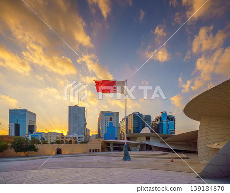 Doha, Qatar - Jan 06 2024, a view of flagpole with the flag of Qatar, fluttering in the wind, with the National Museum of Qatar on background, at evening with cloudy sky, Doha, Qatar Doha, Qatar - Jan 06 2024, a view of flagpole with the flag of Qatar, fluttering in the wind, with the National Museum of Qatar on background, at evening with cloudy sky, Doha, Qatar 139184870