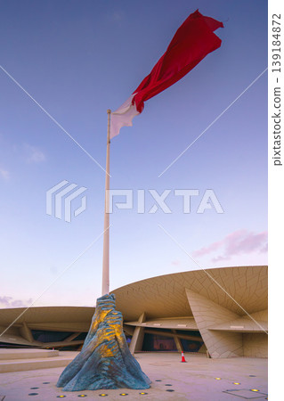 Doha, Qatar - Jan 06 2024, a view of flagpole with the flag of Qatar, fluttering in the wind, with the National Museum of Qatar on background, at evening with cloudy sky, Doha, Qatar Doha, Qatar - Jan 06 2024, a view of flagpole with the flag of Qatar, fluttering in the wind, with the National Museum of Qatar on background, at evening with cloudy sky, Doha, Qatar 139184872
