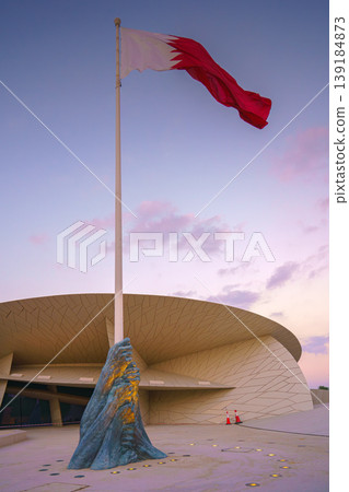 Doha, Qatar - Jan 06 2024, a view of flagpole with the flag of Qatar, fluttering in the wind, with the National Museum of Qatar on background, at evening with cloudy sky, Doha, Qatar 139184873