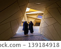 Doha, Qatar - Jan 06 2024, National Museum of Qatar, a view of narrow passage in courtyard with three Arabian woman walking in it, at evening, Doha, Qatar 139184918
