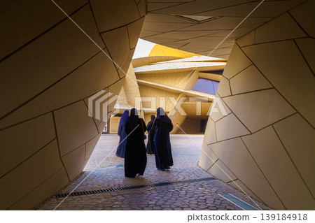 Doha, Qatar - Jan 06 2024, National Museum of Qatar, a view of narrow passage in courtyard with three Arabian woman walking in it, at evening, Doha, Qatar 139184918