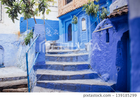 Vibrant blue staircase leads through charming alleyway adorned with colorful walls and lush greenery, showcasing the beauty of traditional architecture and inviting atmosphere 139185299