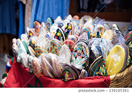 Colorful traditional Moroccan Babouche slippers displayed in a woven basket, showcasing intricate designs and vibrant colors in a market setting Colorful traditional Moroccan Babouche slippers displayed in a woven basket, showcasing intricate designs and vibrant colors in a market setting 139185361