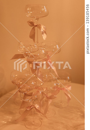 Stacked champagne glasses with pink ribbons arranged elegantly on a table, soft lighting creating a warm ambiance for a celebration or special event Stacked champagne glasses with pink ribbons arranged elegantly on a table, soft lighting creating a warm ambiance for a celebration or special event 139185456