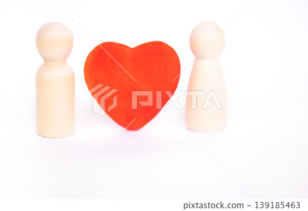Two wooden figurines positioned on either side of a red heart shape, set against a clean white background, symbolizing connection and relationships 139185463