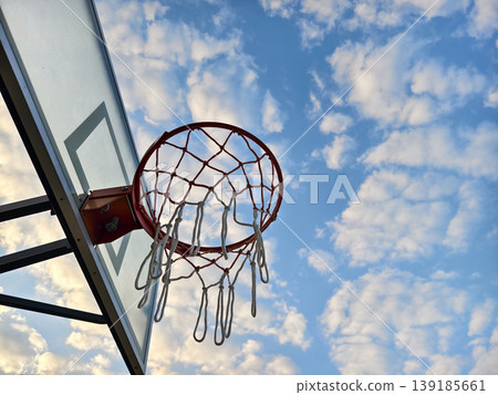 Low angle view of a basketball hoop against a beautiful blue sky with fluffy clouds. 139185661