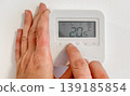 Hands adjusting digital thermostat on white wall at home. Temperature control, energy saving, smart home, climate control, home comfort. 139185854