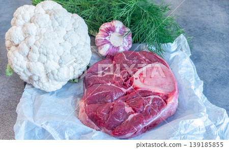 Raw beef shank steak meat with cauliflower garlic dill and cooking ingredients on paper. Rustic kitchen setup for homemade broth, soup and stew preparation. 139185855