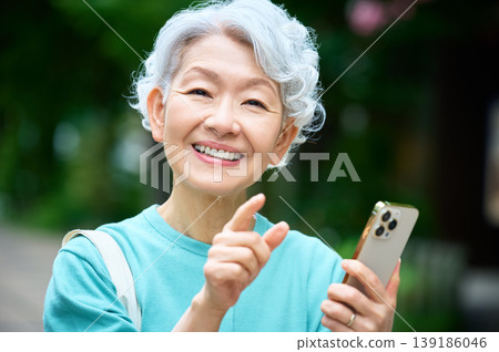 一位精神矍鑠的老婦人面帶微笑，手持智慧型手機指路。 139186046