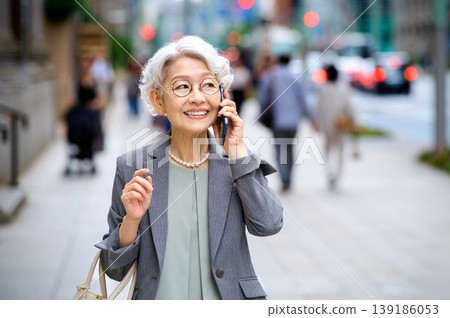 一位活躍的老年女性的都市生活:一邊微笑一邊用智慧型手機通話。 一位活躍的老年女性的都市生活:一邊微笑一邊用智慧型手機通話。 139186053