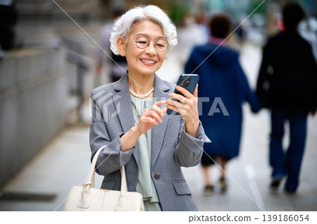 一位老婦人在街上操作智慧型手機時面帶微笑。 139186054