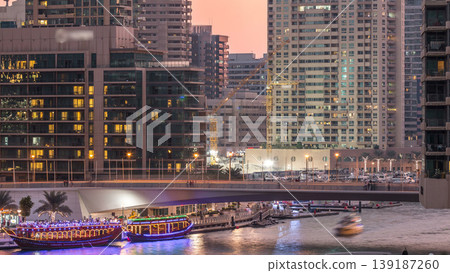 Yachts and boats with tourists staying near shopping mall and passing under a bridge in Dubai Marina district day to night timelapse. Yachts and boats with tourists staying near shopping mall and passing under a bridge in Dubai Marina district day to night timelapse. 139187260